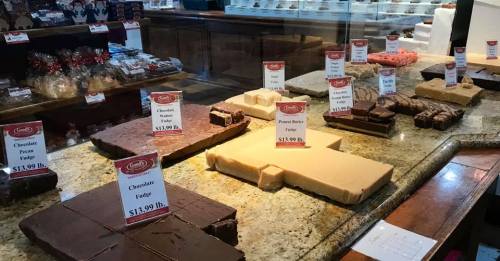 A display of various fudge flavors with price tags, set on a granite countertop in a candy shop.
