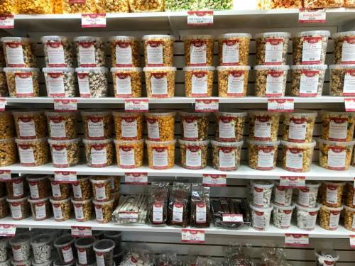 A colorful display of popcorn in clear containers on shelves, labeled with various flavors and prices.