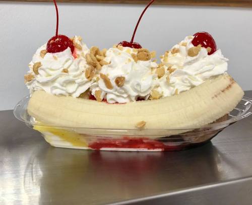 A banana split topped with whipped cream, chopped nuts, and cherries, served in a clear dish.
