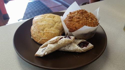 A plate with a scone, a muffin topped with crumbs, and a pastry filled with jam, dusted with powdered sugar.