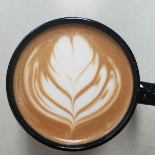 A close-up of a black coffee cup with intricate latte art resembling a leaf on top of creamy coffee.