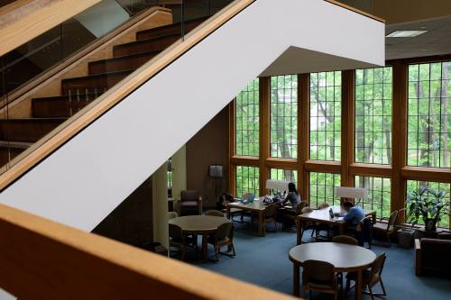A modern library interior with large windows, wooden accents, and people studying at tables.