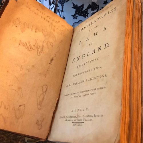 Open book titled "Commentaries on the Laws of England" by William Blackstone, showing aged pages and handwritten notes.