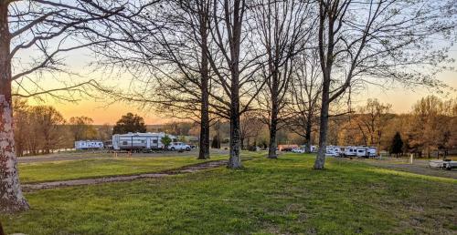 A serene campsite at sunset, featuring RVs parked among bare trees and grassy areas.