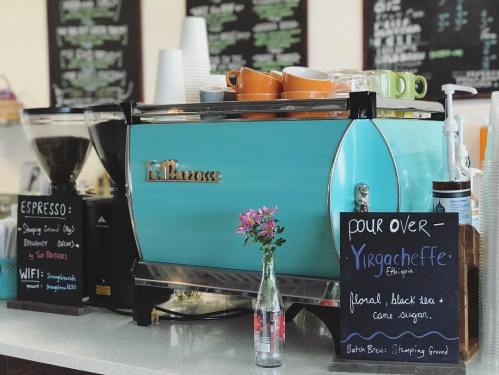 A turquoise coffee machine with cups on top, surrounded by coffee beans and a small flower vase.