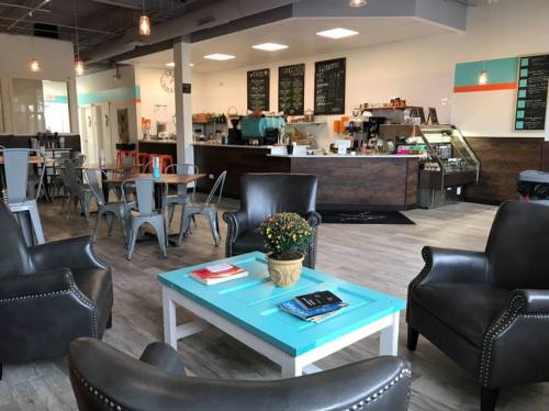 Cozy café interior with seating, a turquoise table, and a counter displaying food and drinks. Bright and inviting atmosphere.