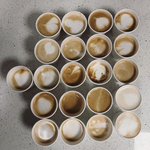 A grid of coffee cups with varying latte art designs, mostly featuring heart shapes on a speckled countertop.