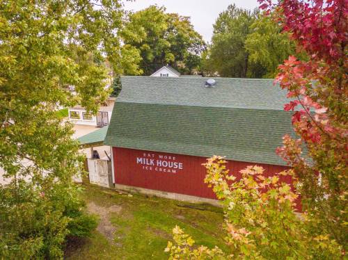 A red barn with a green roof, featuring a sign that reads "Eat More Milk House Ice Cream," surrounded by trees.