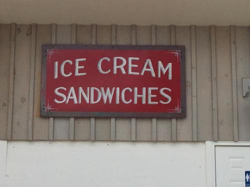Red sign on a wooden wall displaying the words "ICE CREAM SANDWICHES" in bold white letters.
