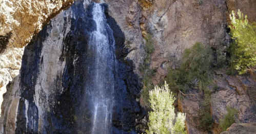 A waterfall cascading down rocky cliffs, surrounded by lush greenery and rugged terrain.