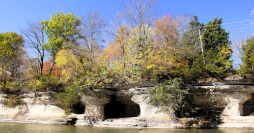 A scenic view of rocky cliffs with caves, surrounded by colorful autumn trees and a clear blue sky.