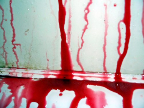 Red liquid streaks down a white surface, creating a dramatic contrast with droplets and a slightly grimy background.