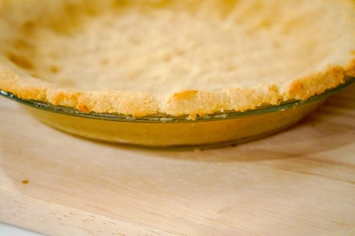 A close-up of a baked pie crust in a glass dish, resting on a wooden surface.