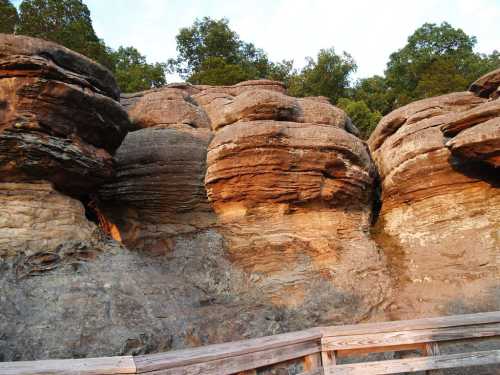 Rock formations with layered textures and greenery above, alongside a wooden walkway.