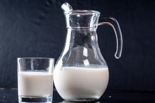 A glass pitcher filled with milk next to a glass of milk on a dark background.