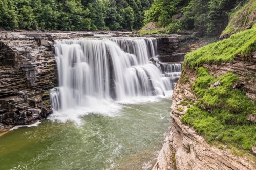 A cascading waterfall flows over rocky cliffs, surrounded by lush greenery and a serene pool below.