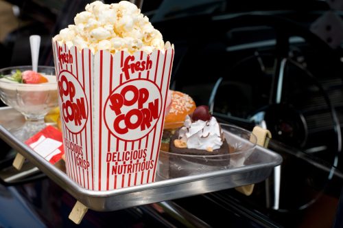 A tray with a large popcorn bucket, a dessert with whipped cream, and a bowl of strawberries.