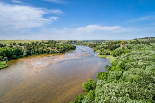 A scenic view of a river winding through lush greenery under a blue sky with scattered clouds.