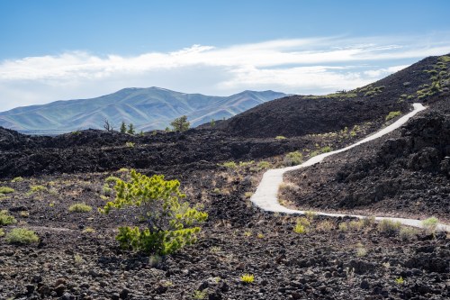 A winding path through a rocky landscape with sparse vegetation and distant mountains under a blue sky.