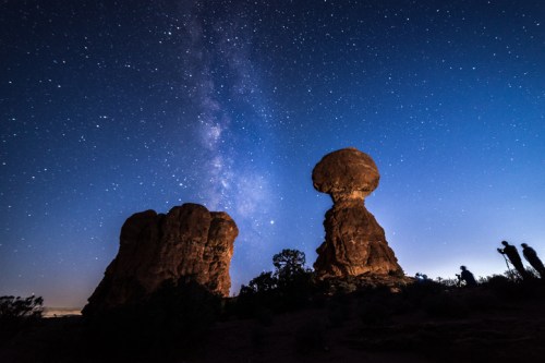 Silhouettes of rock formations under a starry sky with the Milky Way visible in the background.