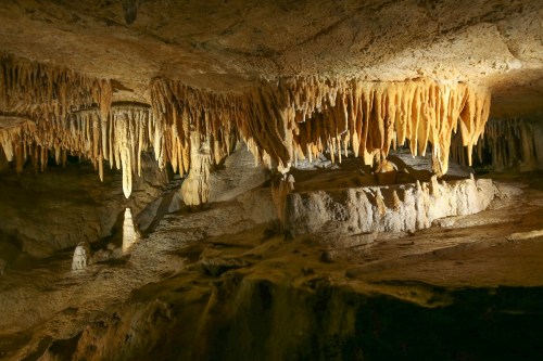 Stalactites and stalagmites in a dimly lit cave, showcasing unique rock formations and textures.