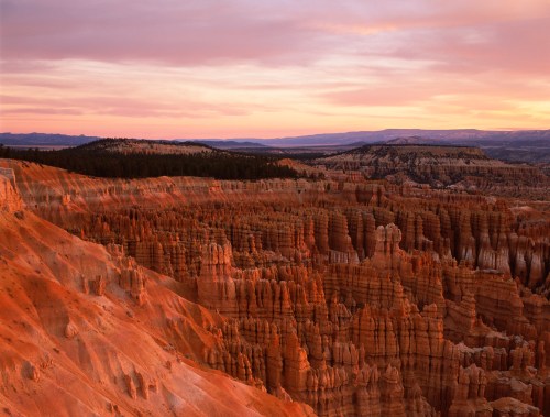 Sunset over Bryce Canyon, showcasing vibrant orange rock formations and hoodoos against a colorful sky.