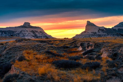 Sunset over rugged cliffs and grassy plains, with vibrant orange and blue hues in the sky.