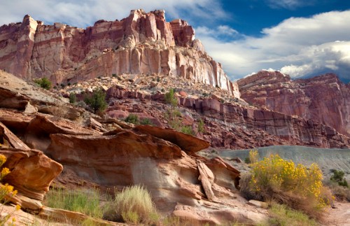 A rugged landscape featuring colorful rock formations and scattered vegetation under a blue sky with clouds.