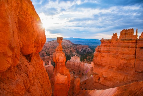 Sunrise over Bryce Canyon, highlighting unique rock formations and vibrant orange hues against a cloudy sky.