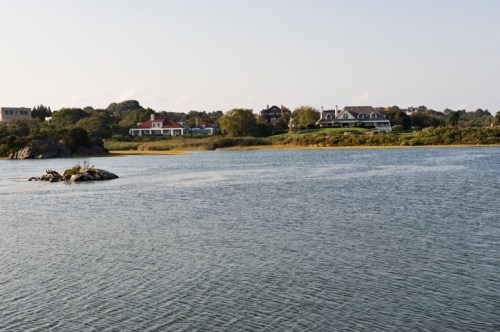 A serene waterfront view featuring houses along the shore and a small rock in the water.