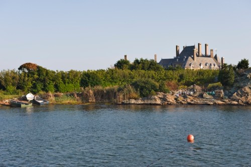 A serene waterfront scene featuring a house on a hill, surrounded by greenery and a small boat near the shore.