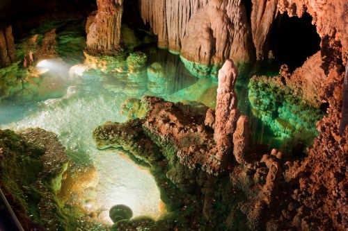 A stunning underground cave with crystal-clear water, illuminated by soft lights, showcasing unique rock formations.