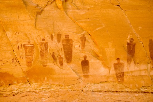 Ancient rock art depicting human figures and symbols on a textured orange sandstone surface.