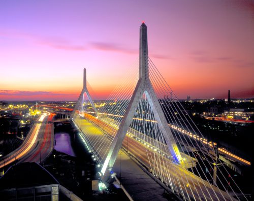 A suspension bridge at sunset, with vibrant colors in the sky and light trails from vehicles below.