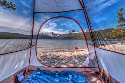 View from inside a tent overlooking a serene lake and snow-capped mountains under a clear blue sky.