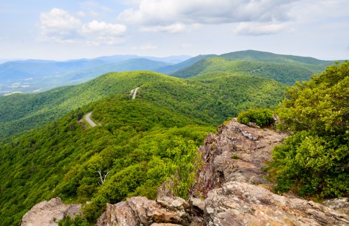A scenic view of lush green mountains and winding roads under a partly cloudy sky.