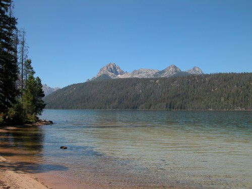 A serene lake surrounded by mountains and pine trees under a clear blue sky.