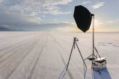A photography setup on a vast, white salt flat with a softbox and tripod against a scenic sky.