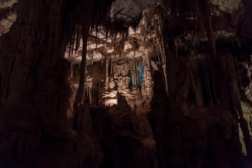 A dimly lit cave interior featuring stalactites and stalagmites, with a blue light illuminating the rock formations.