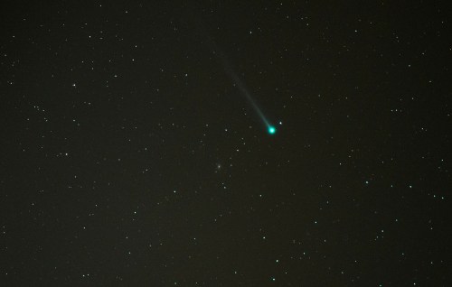 A bright comet with a glowing tail streaks across a star-filled night sky.