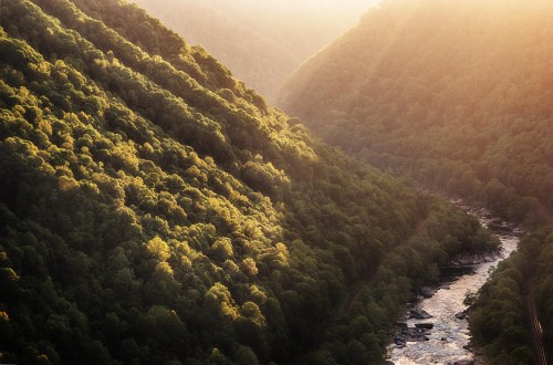 A serene river flows through lush green mountains, illuminated by soft sunlight in a tranquil landscape.