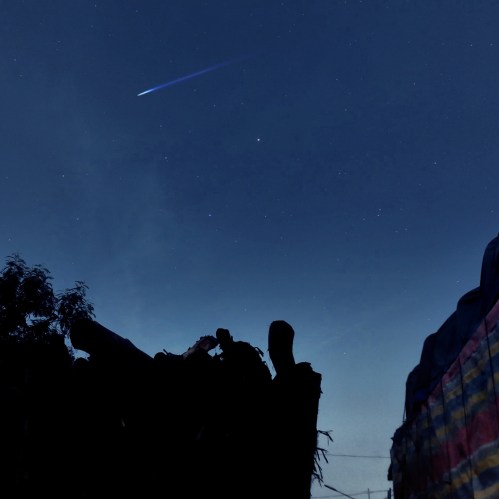 A silhouette of a person against a night sky filled with stars and a bright comet streaking across.