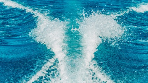 Waves and spray from a boat's wake on a vibrant blue ocean.