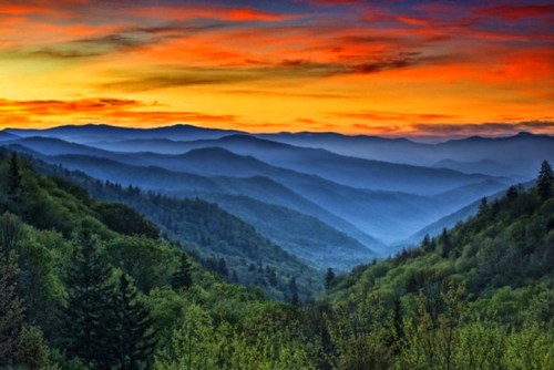 A stunning sunset over layered mountains, with vibrant orange and purple skies and lush green valleys below.