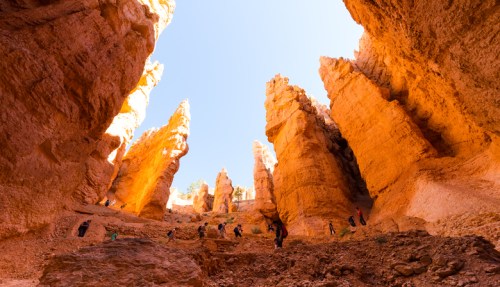 A stunning canyon with towering rock formations and visitors exploring the vibrant landscape under a clear blue sky.