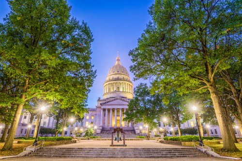 The West Virginia State Capitol building at dusk, surrounded by trees and illuminated by streetlights.