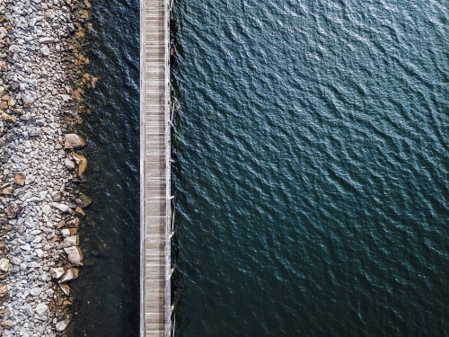 Aerial view of a wooden pier extending over calm water, with rocky shoreline on one side.