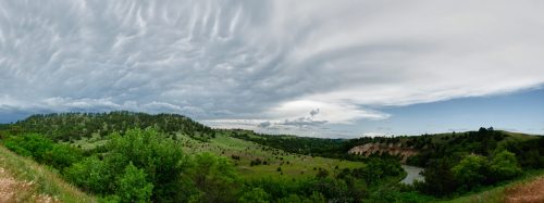A panoramic view of rolling green hills under a dramatic sky with swirling clouds and a winding river.