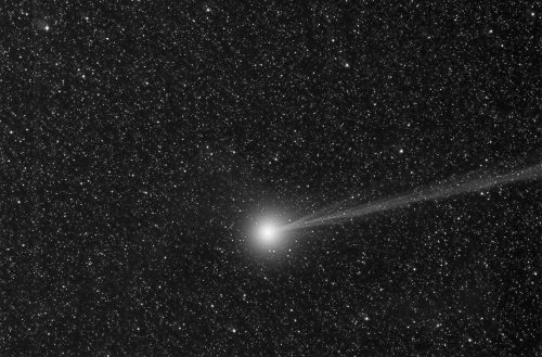 A bright comet with a long tail against a backdrop of countless stars in a dark sky.
