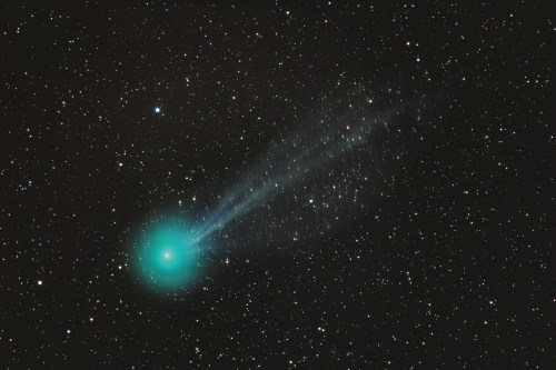 A bright turquoise comet with a long tail, surrounded by a star-filled night sky.
